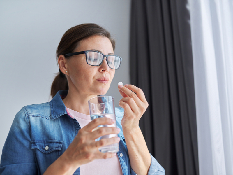 Kvinne med pille og glass vann i hånden